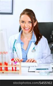 Smiling medical doctor woman sitting at office table and working on computer&#xA;