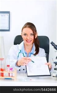 Smiling medical doctor woman sitting at office table with document and pen for signing &#xA;