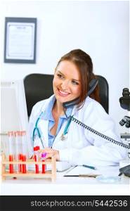 Smiling medical doctor woman talking on phone and looking in monitor&#xA;