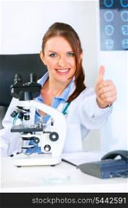 Smiling medical doctor woman using microscope in laboratory and showing thumbs up gesture&#xA;