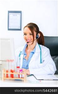 Smiling medical doctor woman with headset sitting at office table and working on computer&#xA;