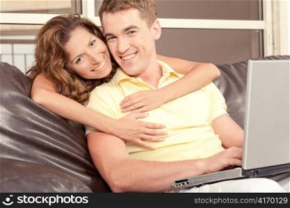 Smiling mid-adult couple opearting laptop and looking at camera