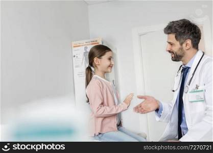 Smiling mid adult doctor shaking hands with girl patient at hospital
