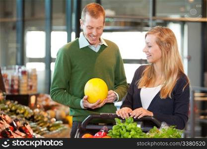 Smiling mid adult man holding fruit while standing with woman in shopping store