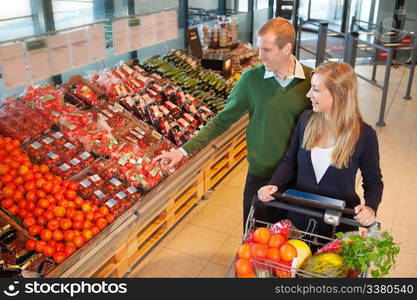 Smiling mid adult man pointing at vegetables while shopping with wife in grocery store