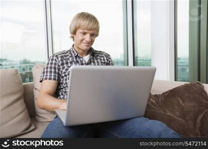 Smiling mid-adult man using laptop on sofa at home