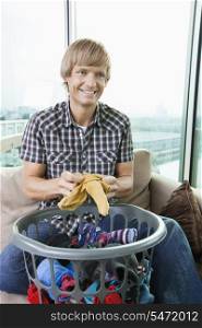 Smiling mid-adult man with laundry basket sitting on sofa at home