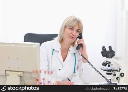 Smiling middle age doctor woman speaking phone at office