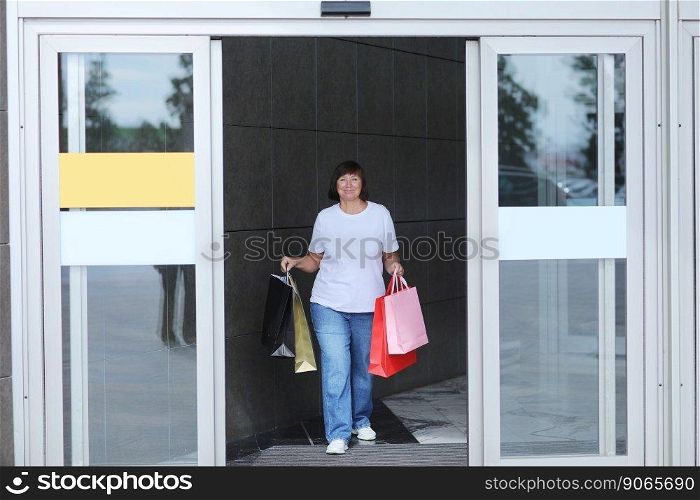 Smiling middle aged woman in casual clothes is walking with colourful shopping bags from shopping mall during Black Friday shopping process, consumerism concept, sale, Season winter summer sales.. Smiling middle aged woman in casual clothes is walking with colourful shopping bags from shopping mall during Black Friday shopping process, consumerism concept, sale, Season winter summer sales