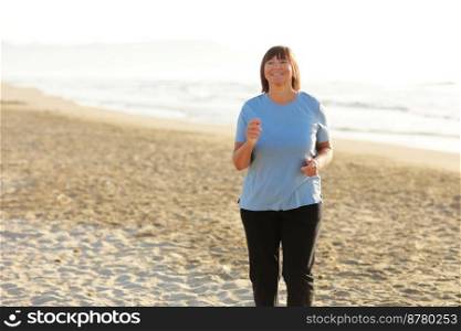 Smiling middle aged woman running on the beach on sunrise. 40s or 50s attractive mature lady in sports clothes doing jogging workout enjoying fitness and healthy lifestyle at beautiful sea landscape. Smiling middle aged woman running on the beach on sunrise. 40s or 50s attractive mature lady in sports clothes doing jogging workout enjoying fitness and healthy lifestyle at beautiful sea landscape.