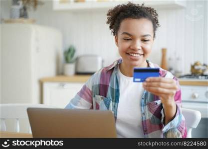 Smiling mixed race girl ecommerce client using bank credit card to make electronic payment on laptop. Happy young lady shopping online on computer using banking services at home. E-banking.. Smiling mixed race girl using credit card shopping on laptop, using online banking services at home