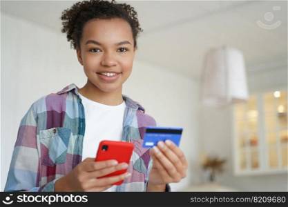 Smiling mixed race girl holding credit card and smartphone, using online banking services, e-bank mobile apps. Happy teen biracial lady paying purchase, making secure bank money transfer at home.. Smiling mixed race girl holding bank credit card, use online banking services, e-bank mobile apps