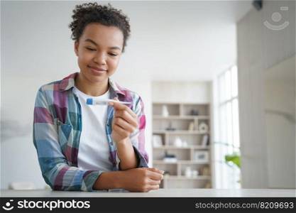 Smiling mixed race teen girl holds digital thermometer, pleased with normal body temperature after treatment at home. Satisfied biracial young woman checking temp during covid pandemic.. Smiling mixed race teen girl holds thermometer pleased with body temperature after treatment at home