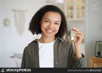 Smiling mixed race teen girl tenant or homeowner holds keys to new home apartment, happy young biracial lady renter holding house key, standing indoors. Rental housing, mortgage advertisement.. Smiling mixed race teen girl tenant or homeowner holds keys to new home. Rental housing, mortgage