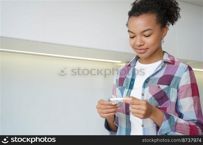 Smiling mixed race young girl holds digital thermometer, checking body temperature before trip during coronavirus pandemic. Calm satisfied teen lady measuring temp, has no fever, covid symptom.. Mixed race young girl holds thermometer, checking body temperature before trip during covid pandemic