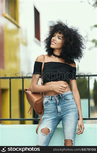 Smiling mixed woman with afro hair standing on the street. Female wearing casual clothes in outdoors. Lifestyle concept. Smiling mixed woman with afro hair standing on the street