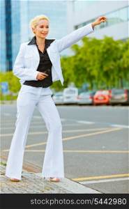 Smiling modern business woman catching taxi near office center&#xA;