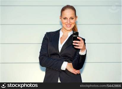 Smiling modern business woman holding mobile in hand near office building &#xA;
