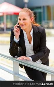 Smiling modern business woman leaning on railing and talking on mobile&#xA;