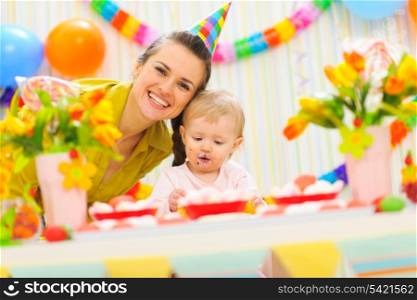 Smiling mom and eat smeared baby on birthday celebration party