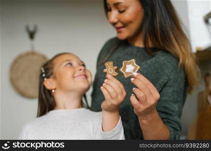 Smiling mom and her daughter are holding Christmas cookies in their kitchen