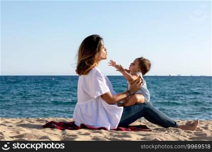 Smiling mommy playing with newborn lying on beach towel
