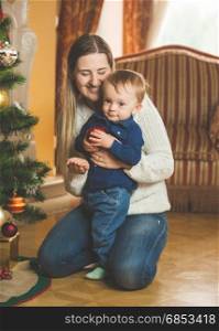 Smiling mother and baby boy decorating Christmas tree with baubles