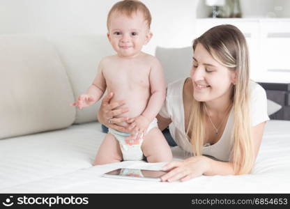 Smiling mother and baby boy using digital tablet on bed
