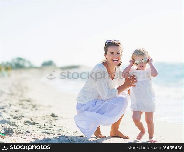 Smiling mother and baby wearing sunglasses on beach