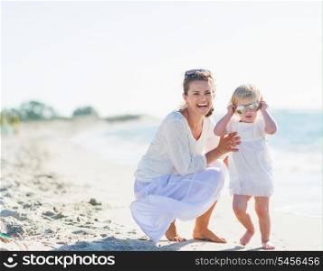 Smiling mother and baby wearing sunglasses on beach