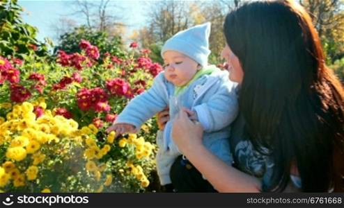 Smiling mother and child near a flowerbed in a sunny autumn day