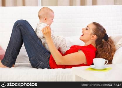 Smiling mother and cute baby playing on divan