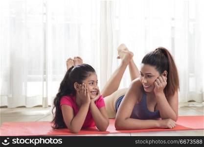 Smiling mother and daughter lying on yoga mat