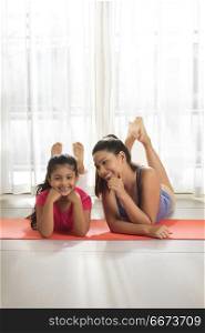 Smiling mother and daughter lying on yoga mat