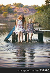 smiling mother and daughter sitting on the pier warm autumn day dangling his legs in the water and splash in the foreground