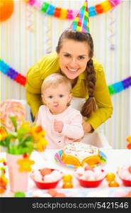 Smiling mother and eat smeared baby on birthday celebration party