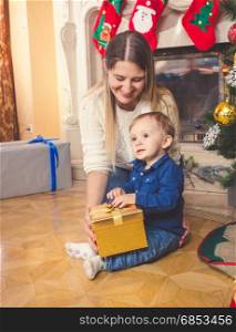 Smiling mother and her baby son with Christmas gift on floor at living room