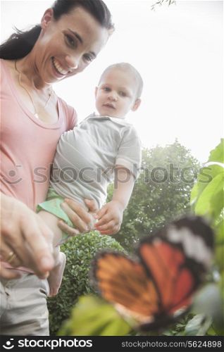 Smiling mother and son pointing and looking at a butterfly in the garden