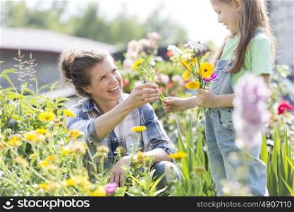 Smiling mother giving flowers to daughter while gardening at farm