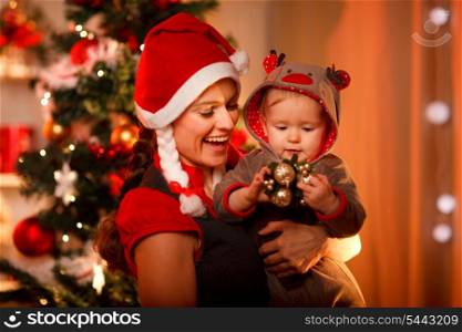 Smiling mother playing with lovely baby near Christmas tree&#xA;