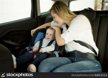 Smiling mother sitting on car backseat with her baby