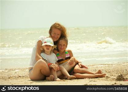smiling mother with her children are sitting on a beach.