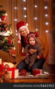 Smiling mother with lovely baby sitting near Christmas tree&#xA;
