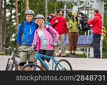 Smiling mountain bikes couple and hikers waiting after chair lift trip