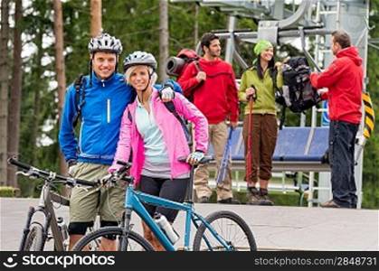 Smiling mountain bikes couple and hikers waiting after chair lift trip