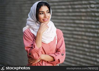 Smiling Muslim woman wearing hijab headscarf walking in the city center. Arab female in urban background. Young Arab woman wearing hijab headscarf walking in the city center.