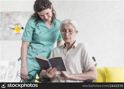 smiling nurse looking book hold by female senior patient sitting wheel chair