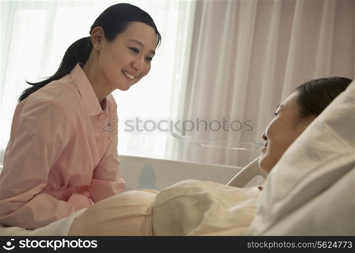 Smiling nurse talking to pregnant woman lying on bed in the hospital