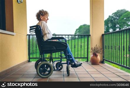 Smiling older woman in a wheelchair in the porch. Older woman in a wheelchair