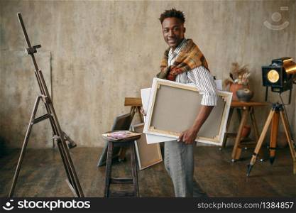 Smiling painter with canvas standing in art studio. Male artist draws at his workplace, creative master works in workshop. Smiling painter with canvas standing in art studio